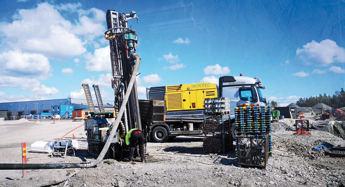 Image of a driller drilling a thermal well, with Rototec's compressor in the background.